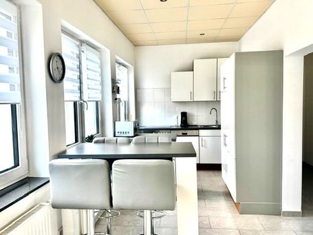 Freundliche, moderne Küche mit weißen Schränken, einer schwarzen Arbeitsplatte und einer gemütlichen Frühstücksbar mit vier Barhockern