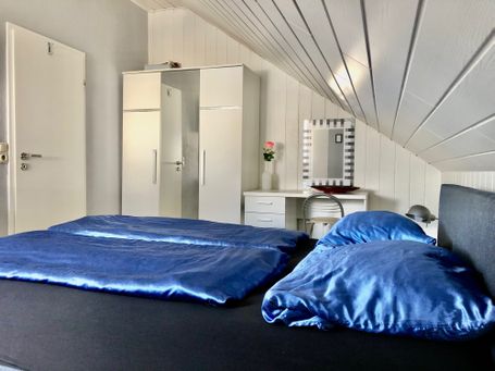Modern eingerichtetes Schlafzimmer mit Doppelbett in dunklem Design, blauen Satin-Bettbezügen und einem großen Kleiderschrank. 