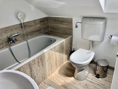 Geschmackvoll gestaltetes Badezimmer mit Badewanne, Toilette und Waschbecken unter einer Dachschräge. 