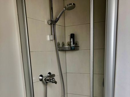 Moderne, platzsparende Duschkabine mit verstellbarem Duschkopf und Glaswänden. Die hellen Fliesen sorgen für eine freundliche Atmosphäre.