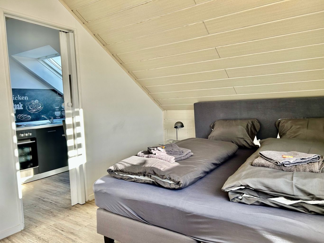 Geschmackvoll eingerichtetes Schlafzimmer im Dachgeschoss mit einem großen Doppelbett in dunklen Grautönen. 