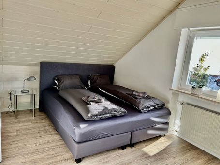 Elegantes Schlafzimmer im Dachgeschoss mit einem großen Doppelbett in dunklen Grautönen. 
