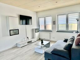Stilvoll eingerichtetes Wohnzimmer mit großer grauer Couch, Flachbildfernseher an der Wand, modernem weißen Wohnzimmertisch