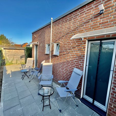 Große, gepflasterte Terrasse mit mehreren bequemen Liegestühlen und Sitzmöglichkeiten an einer modernen Backsteinfassade. 