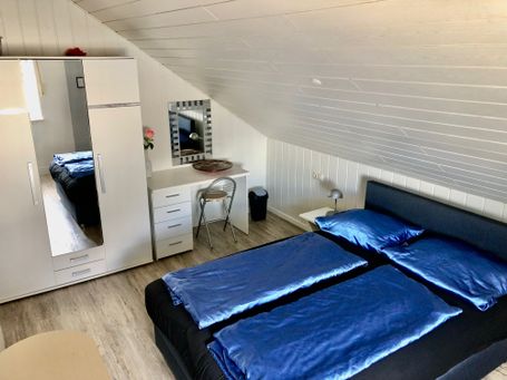 Stilvoll eingerichtetes Dachgeschoss-Schlafzimmer mit Doppelbett, Kleiderschrank mit Spiegel, Schreibtisch und heller Holzverkleidung.
