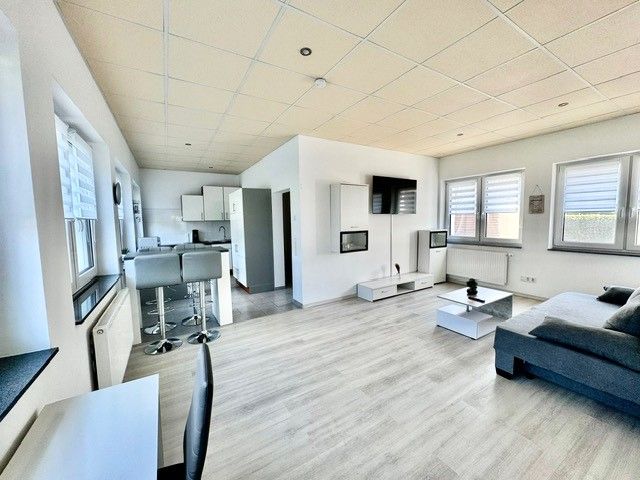 Helles und modern eingerichtetes Gästezimmer mit offener Küche, Barhockern, gemütlicher Couch und Flachbildfernseher.