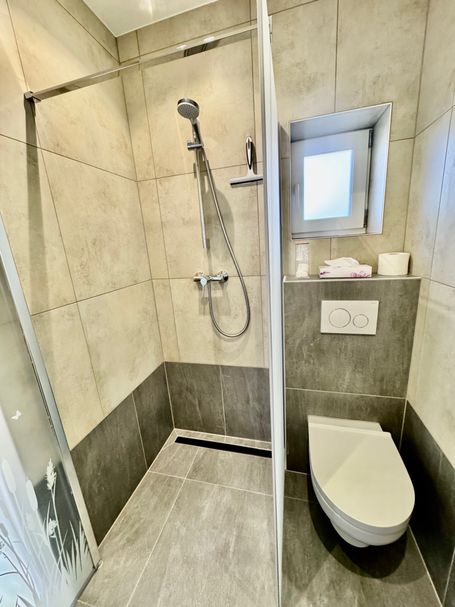 Modern gefliestes Badezimmer mit ebenerdiger Dusche, stilvoller Glasabtrennung und wandhängendem WC. 